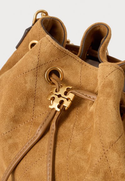 Gros plan d'un sac en daim beige à cordon avec œillets métalliques dorés et une attache décorative dorée sur des cordons en cuir.