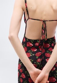 Μαύρο φόρεμα με floral σχέδιο, που δένει στο πίσω μέρος, με μοτίβο κόκκινης τριανταφυλλιάς, λεπτές τιράντες και εφαρμοστή γραμμή, με ομαλή υφή υφάσματος.