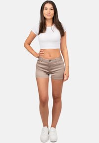 Beige denim shorts met een strakke pasvorm, vijf zakken en een knoopsluiting, gecombineerd met een witte cropped t-shirt en witte sneakers.