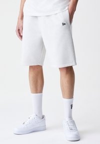 White cotton blend shorts with an elastic waistband and side pockets, featuring a small black logo accent. Paired with white sneakers and socks.