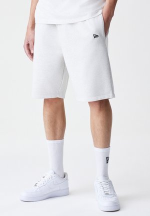 Pantalones cortos de mezcla de algodón blancos con cintura elástica y bolsillos laterales, con un pequeño acento de logo negro. Combinados con zapatillas blancas y calcetines.