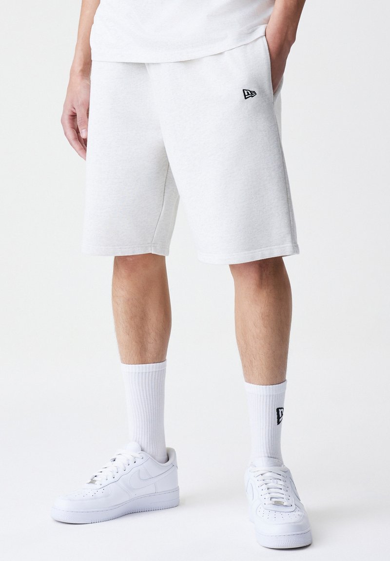 White cotton blend shorts with an elastic waistband and side pockets, featuring a small black logo accent. Paired with white sneakers and socks.