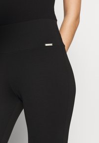 Leggings neri con una vita alta, realizzati in materiale elasticizzato. Presentano un piccolo logo argentato sulla vita.