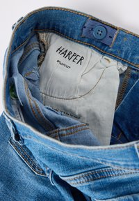 Siniset bootcut farkut, joissa on ruskeasti ommeltu vyötärönauha, sininen nappi ja "HARPER"-merkki. Sisäpinta on kevyttä kangasta.