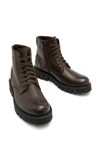 Brązowe skórzane botki za kostkę o teksturowanym wykończeniu, z przodem na sznurówki i bocznym zamkiem błyskawicznym, osadzone na grubej czarnej gumowej podeszwie.