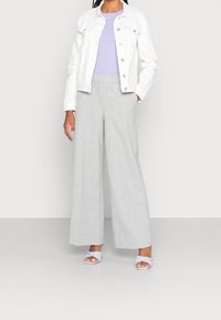 Biała kurtka dżinsowa z srebrnymi guzikami, fioletowa bluzka z krótkim rękawem, jasnoszare spodnie szerokie, oraz lawendowe klapki.