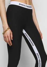 Svarta leggings med ett vitt elastiskt midjeband som har "paco rabanne"-logotypen. Sidofickor har kontrasterande vita ränder med text.