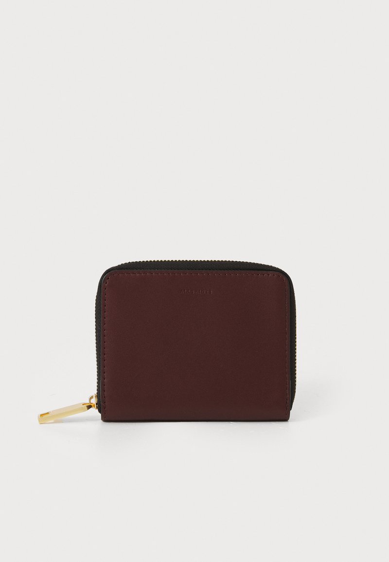 Portafoglio compatto con esterno in pelle bordeaux, zip dorata e bordi in tessuto nero. Presenta una texture semplice e liscia.