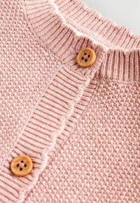 Rosa gestrickte Strickjacke mit einem gerippten Kragen und Holzknöpfen, die ein strukturiertes Muster im ganzen Stoff aufweist.