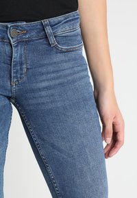 Džíny z denimu ve středně modré barvě se štíhlým střihem, pěti kapsami, zapínáním na knoflíky a jemným prošisováním na stehnech.