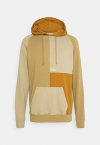 Sweat à capuche présentant un design en blocs de couleurs beige et moutarde, en coton, avec une poche kangourou et un détail logo à l'avant.