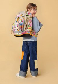 Mehrfarbiger Rucksack mit Punkten, beigem Grund und Fronttasche. Gestylt mit Patches auf Jeanshosen und aufgerollten Säumen.
