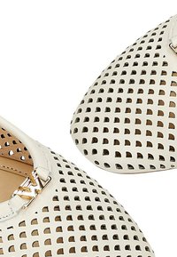 Skórzane buty wsuwane z perforowanym wzorem w kolorze białym, zdobione metalowymi elementami. Okrągły nosek i płaska podeszwa.