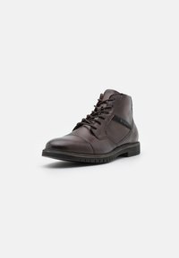 Bruna läderankelboots med rund tå, snörning framtill och en distinkt logotypaccent. Har en strukturerad gummisula för bättre grepp.