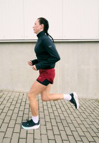 Jooksuriietus: must pika varrukaga pluus ja punased lühikesed püksid. Mustad spordijalatsid valgete tallatega. Punutud juuksed. Jooksmine sillutatud pinnal.