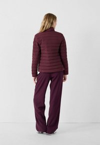 Bordeauxkleurige pufferjack met verticale gestikte patroon, hoge kraag en rekbare broek in bijpassende kleur, beiden op maat gemaakt voor comfort.