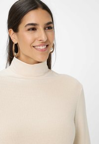 Beige ribbet turtle neck sweater med en tætsiddende pasform. Har lange ærmer og en blød tekstur, suppleret af store hoops øreringe.