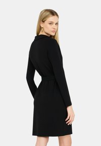 Abito nero con maniche lunghe, collo a camicia, vestibilità slim e vita con cintura. Tessuto liscio con orlo all'altezza del ginocchio.
