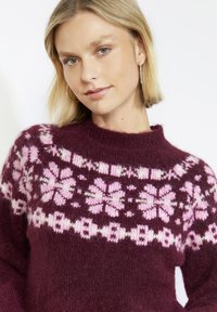 Burgundský pletený sveter s ružovým kvetinovým vzorom a snehovou vločkou. Má zaoblený výstrih a mäkkú, textúrovanú látku.