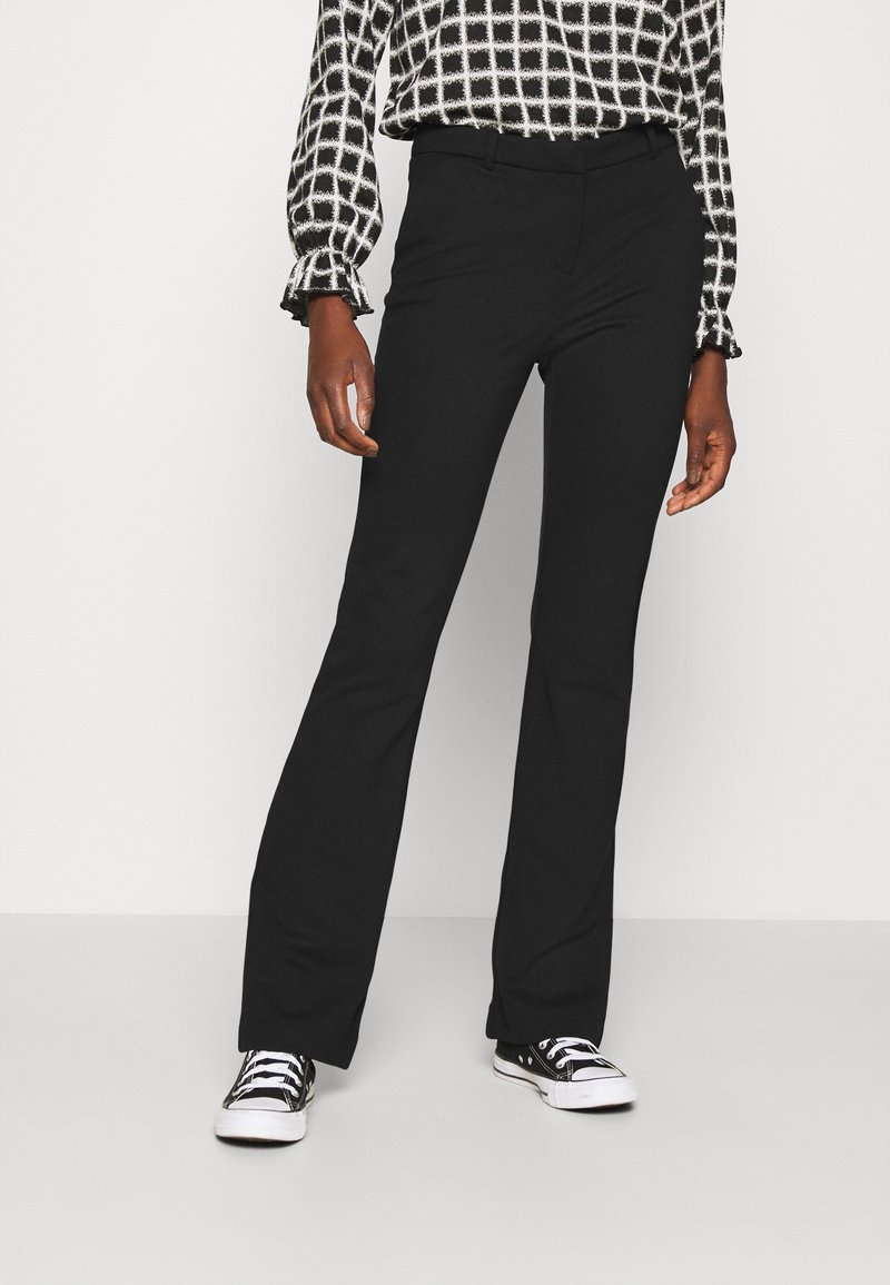 Černé nohavice do zvonu vyrobené z hladkého materiálu, s páskem se středním vzestupem a přizpůsobeným střihem. Kombinované s černobílým kostkovaným topem a teniskami.