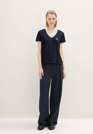 T-shirt navy con scollo a V in tessuto morbido, abbinato a pantaloni navy larghi e comodi. Presenta un design minimalista e un logo discreto sul petto.