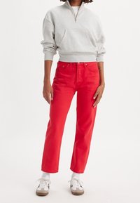 Grå zip-up sweatshirt med framlapp, kombinerad med högmidjade röda jeans. Vita strumpor och avslappnade skor fulländar outfiten.