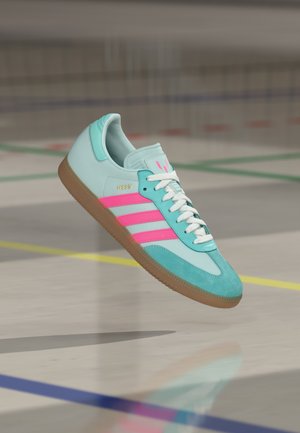 Zapatillas azul claro con rayas rosas, fabricadas en materiales de gamuza y cuero, con cordones planos blancos y suela de goma. Presentan un logo en dorado de "MESSI".