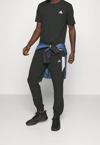 Zwart sport t-shirt met wit logo, gecombineerd met zwarte joggers met witte en paarse accenten. Zwarte sportschoenen maken de look compleet.