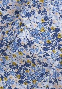 Tissu floral avec un fond blanc. Présente des fleurs bleues, jaunes et roses dispersées. Texture douce, matériau en coton léger.