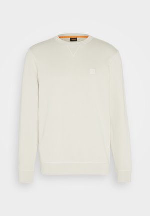 Helles cremefarbenes Sweatshirt mit Rundhalsausschnitt, langen Ärmeln und kleinem quadratischen Logo auf der Brust. Weiche Textur und kontrastierendes oranges Innenfutter.