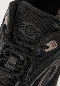 Černá atletická bota vyrobená z kombinace síťoviny a kůže. Výrazné detaily zahrnují texturovaný vzor, výrazné logo a texturované tkaničky.