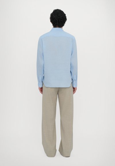 Chemise bleu clair à manches longues avec une coupe droite et des détails de boutons, associée à un pantalon ample beige, tous deux fabriqués à partir de tissus doux.