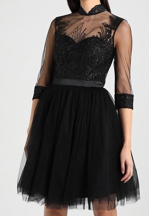 Vestido negro hasta la rodilla con mangas largas transparentes, detalles de encaje y lentejuelas en el corpiño, cuello alto y una cinturilla satinada.