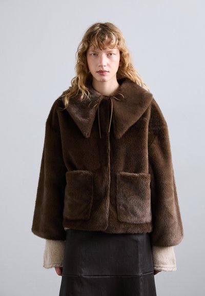 Veste en fausse fourrure marron avec un large col, deux poches avant et une fermeture à nouer. Les manches longues présentent un détail tricoté de couleur claire contrastant.