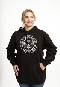 Sudadera con capucha negra que presenta un diseño gráfico con alas y texto. El material parece suave, con un bolsillo delantero y capucha con cordón.