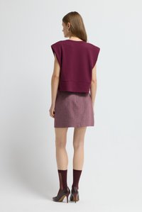 Kvinde står med ryggen til iført en ærmeløs burgunder top, lyserød nederdel, burgunder gennemsigtige strømper og mørkeburgunder høje hæle.