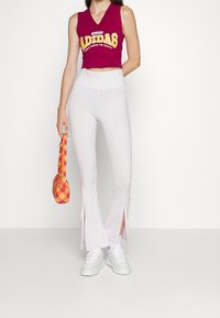 Bordová bezramínková crop top s zlatým logem "Adidas", kombinovaná s bílými legínami s bočními rozparky. Doplňkem je taška v oranžovo-růžovém károvaném vzoru.