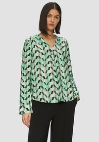 Langsleeve blouse van lichte stof met een geometrisch patroon in groen, zwart en wit. V-hals en een relaxte pasvorm met omgeknoopte mouwen.