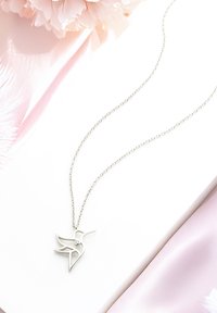 Sølv kolibri vedhæng på en delikat kæde, med et geometrisk design og en lille accentsten, der ligger på en blød pink overflade.