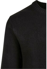 Suéter negro de punto con una textura acanalada, diseño clásico de cuello redondo y detalles mínimos. La tela es suave y ligeramente texturizada.