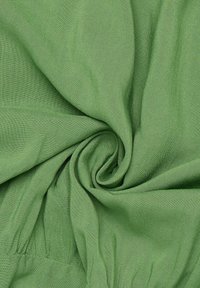 Tessuto verde, morbida texture, materiale leggero, con una finitura liscia, che mostra un motivo a spirale al centro e un bordo semplice.