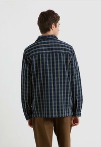 Marinefarbener karierten Hemd mit Button-Down-Kragen, ausgestattet mit beige Kreuzmuster, langen Ärmeln und Manschettenknöpfen. Die Rückansicht zeigt ein Yoke-Nahtdetail.