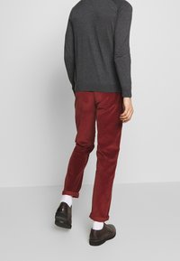 Graues Langarmshirt kombiniert mit burgunderroten Cordhosen, die mit umgeschlagenen Bündchen versehen sind. Dunkelbraune Schuhe mit glatter Oberfläche runden den Look ab.