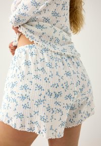 Hvid blomsterkort sæt med tekstureret stof med blå blomster og grønne accenter. Shortsene har en bølget kant og elastisk talje.
