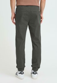 Pantalon gris foncé fuselé avec une taille élastique, deux poches arrière et des poignets élastiques, associé à des baskets blanches avec des accents noirs.