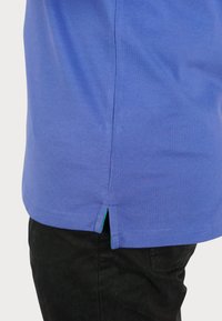 Lilla bomulds t-shirt med lige snit, sidesplits ved sømmen og en kontrasterende grøn detalje indeni splitten.
