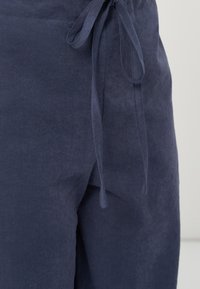 Gros plan sur un pantalon en lin bleu marine avec une ceinture en tissu nouée à la taille et des détails de couture visibles.