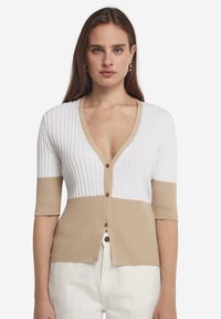 Stickad cardigan med djup V-ringning, med ribbad textur i vitt och beige. Korta ärmar, framknappar och kontrasterande färgblock.