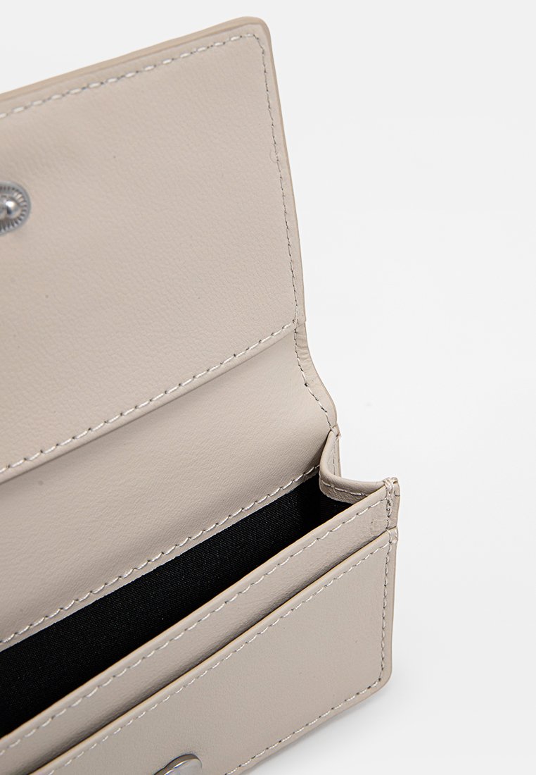 Portafoglio in pelle beige aperto per mostrare l'interno foderato in tessuto nero con chiusura a pulsante metallico argentato, su sfondo bianco.