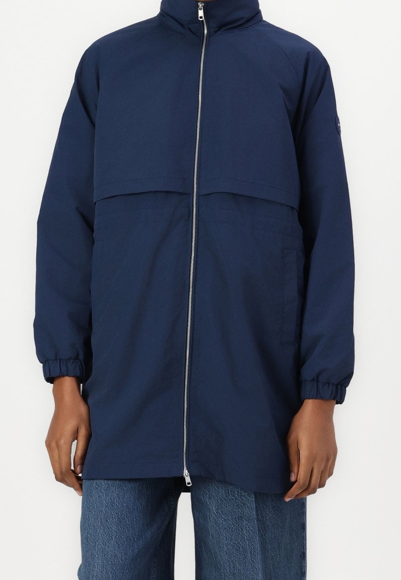 Veste bleu marine avec un col montant, une fermeture éclair à l'avant, des poignets élastiques et une coupe décontractée. Tissu lisse à la texture mate avec des poches latérales.